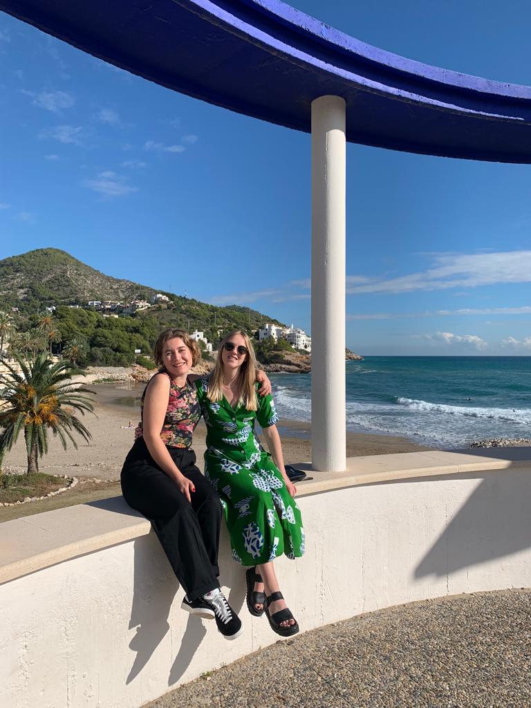 Photo of Hannah and Phil sat on a bench in Sitges, Spain with the Beach behind them during the World Orphan Drug Congress.