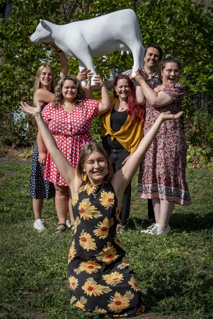 A Photo of the beacon team holding a white fibreglass cow. Mary Rose, Hannah, Freya, Rick and Laura are holding the cow in the air. Phil needs on the floor in front of them with her arms outstretched in celebration.