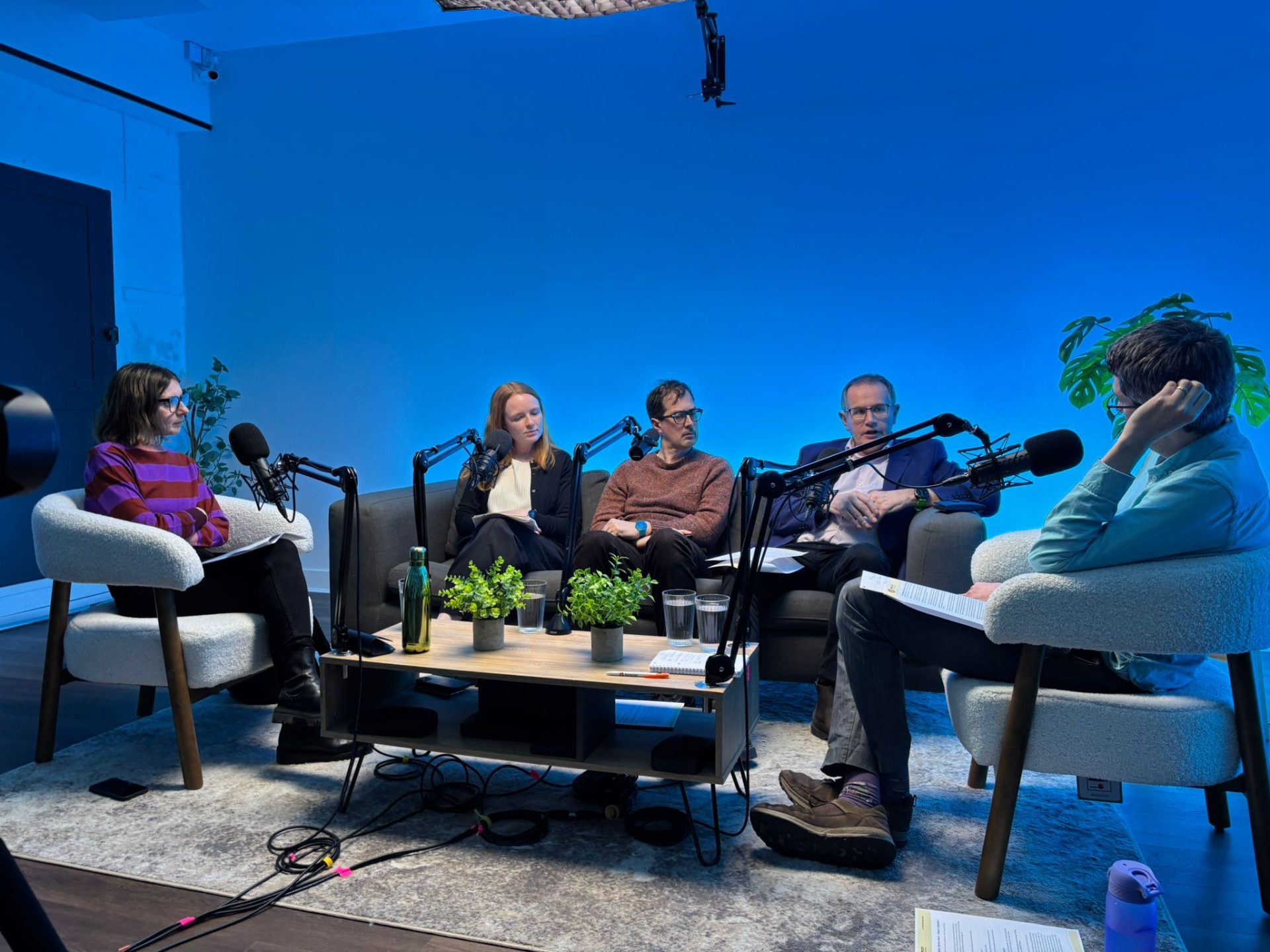 Rick Thompson, Nick Meade, Rosie Lindup, Julian Beach, and Alessandra Gaeta mid-discussion in a podcast studio with blue light.