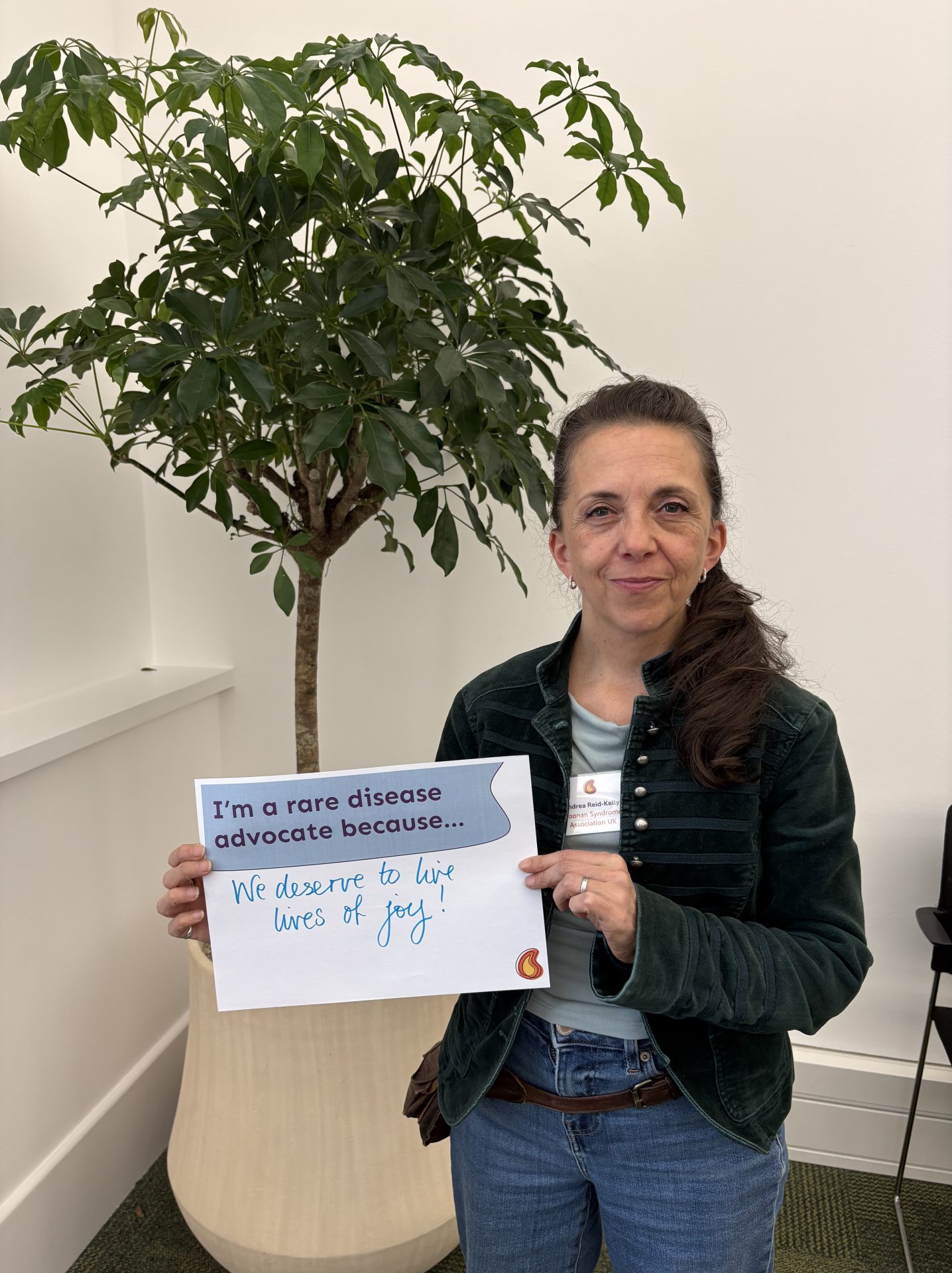 Masterclass attendee holding a sign and smiling. Text reads 'I'm a rare disease advocate because we deserve to live lives of joy'.