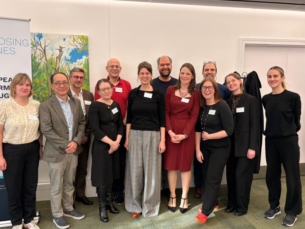 A group photo of 12 multi-stakeholder meeting attendees. They are wearing formal clothing and smiling at the camera.