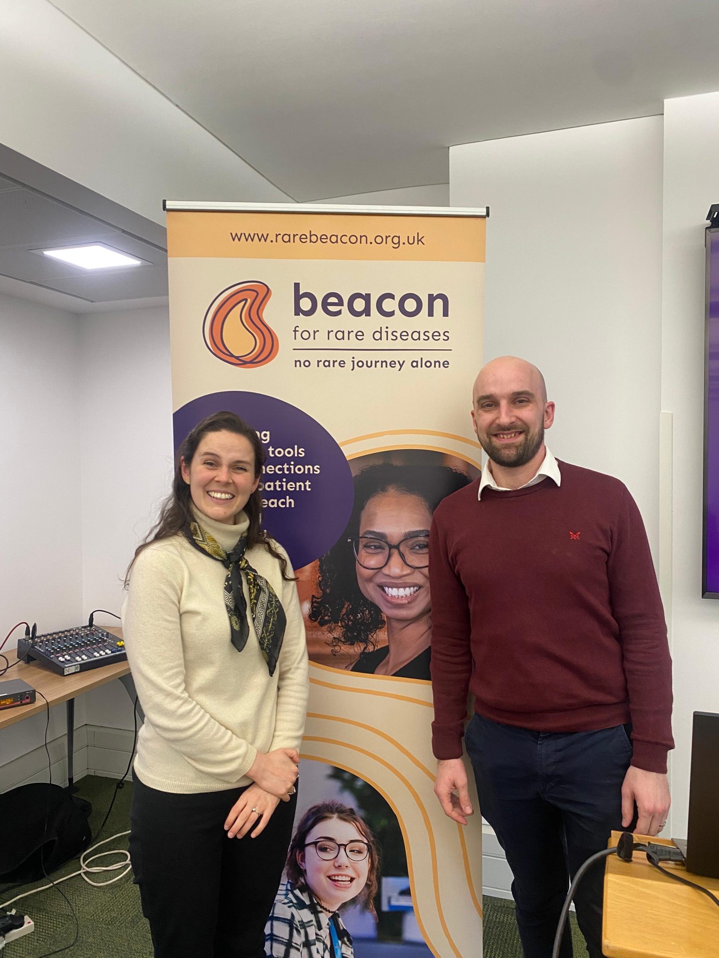 Blayne Baker and Dave Taylor-Langdale stood in front of yellow and purple Beacon-branded banner, smiling at the camera.